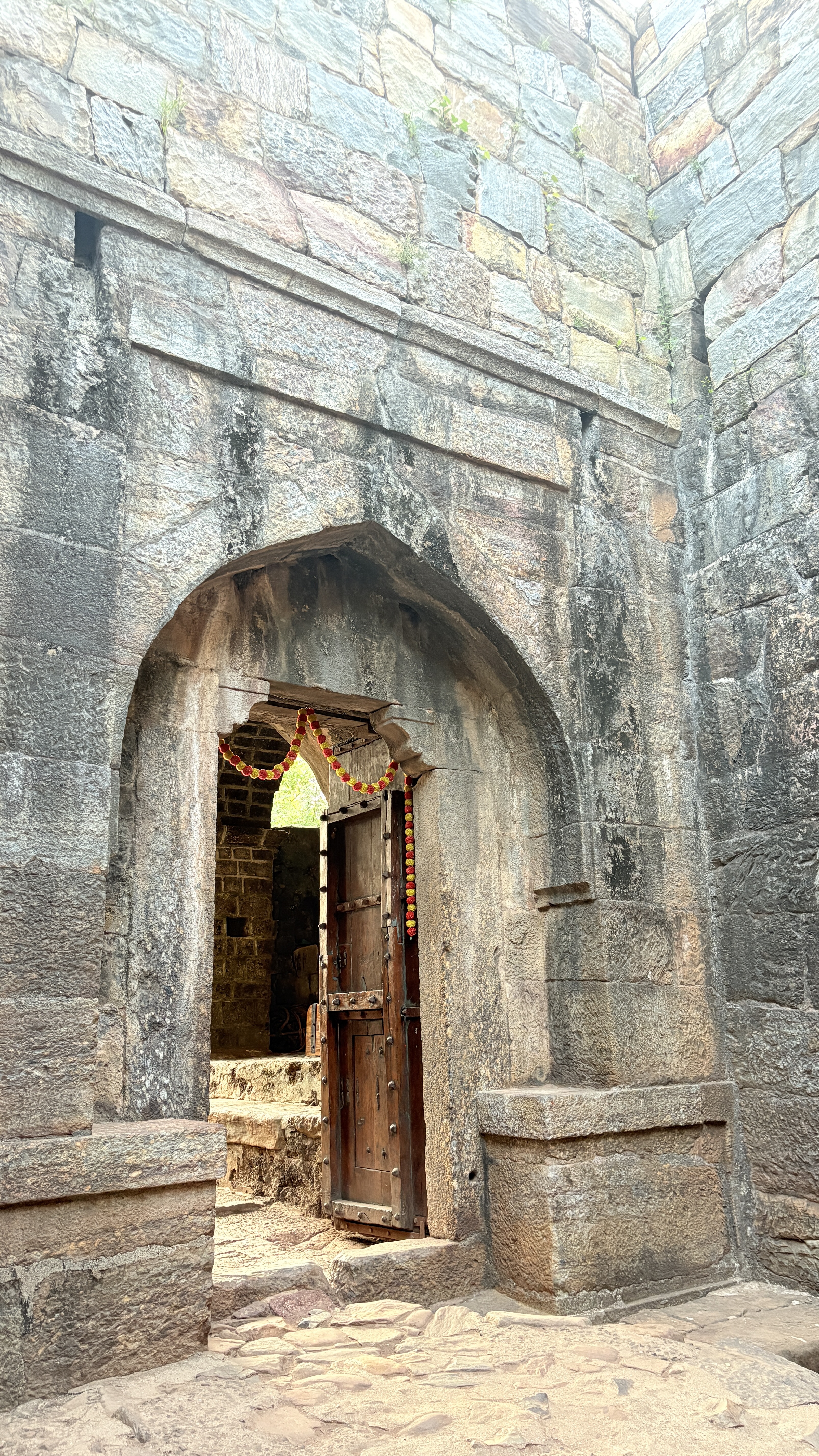 A weathered stone archway leads to an interior space, with a wooden door partially open.