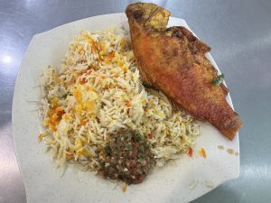 A plate of colorful rice with a whole fried fish and spicy sauce.
