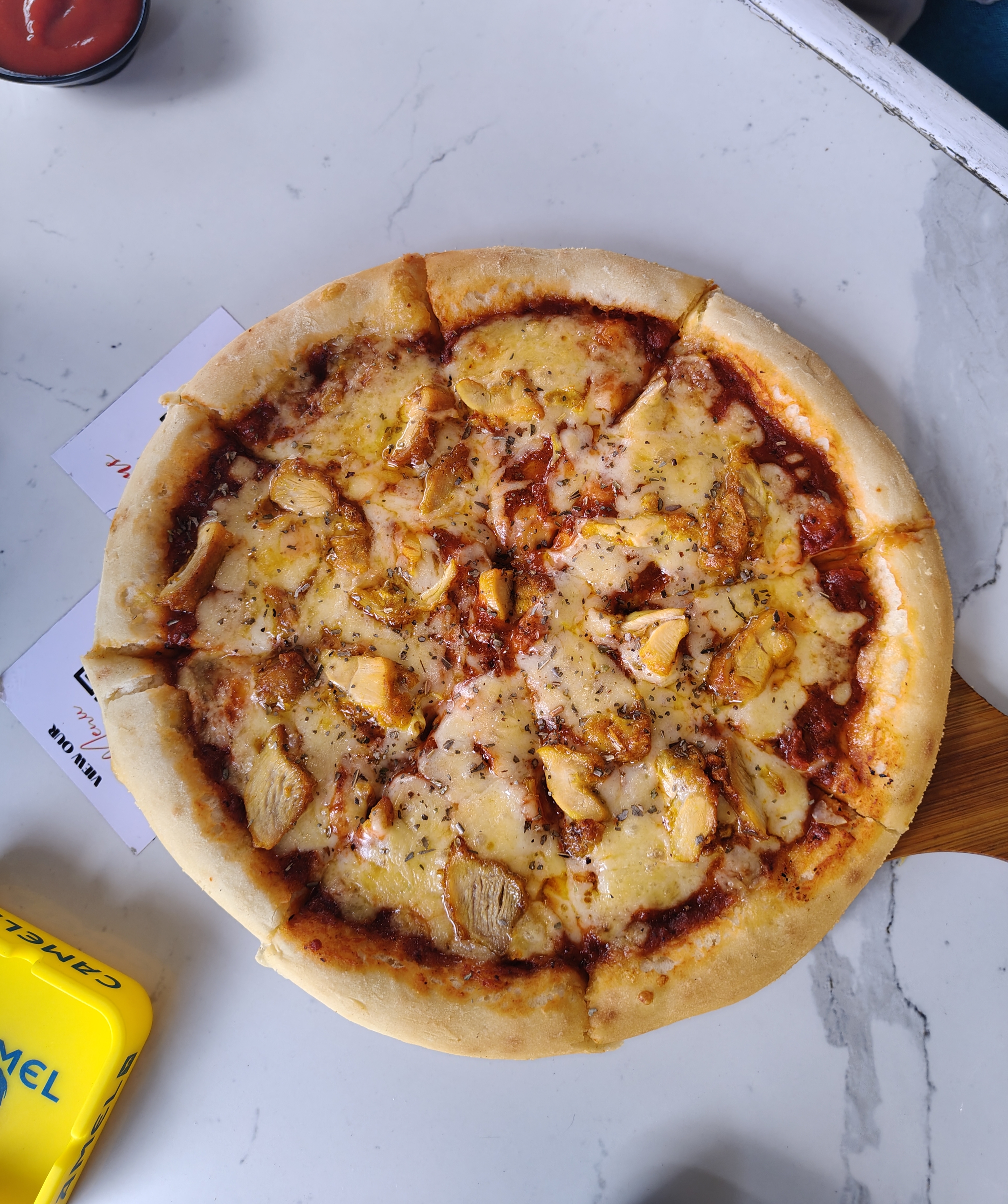 A round pizza sits on a wooden serving board, topped with melted cheese, pieces of chicken, and a rich tomato sauce.