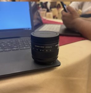 Camera lens sitting on a laptop at tabletop.
