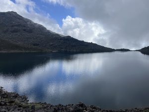 A tranquil mountain lake reflecting the gray sky and surrounding rocky hills.