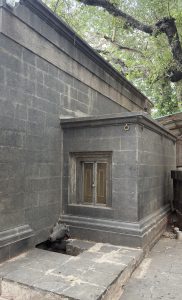 A stone structure with dark grey brickwork and a small window with metallic doors, part of a temple.