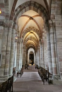 Hallway with arches in a church, with some rows of wooden seats. 