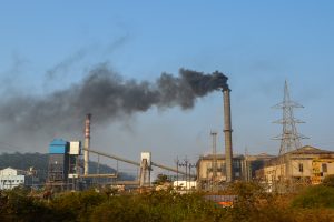 

A large industrial sugar factory featuring multiple structures including smokestacks, a tall chimney emitting dark smoke, and various machinery.