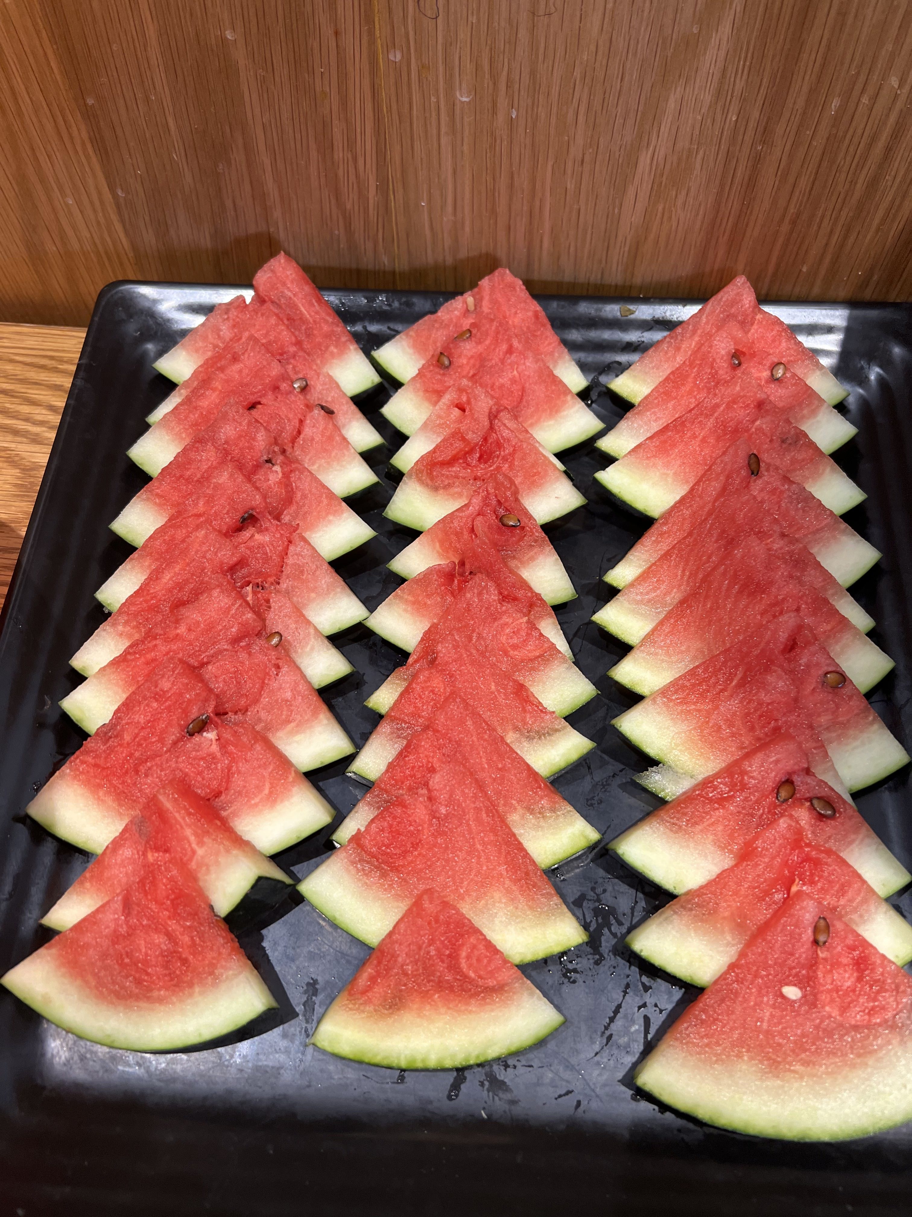 A rectangular black platter holds neatly arranged triangular slices of watermelon.
