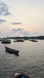 A serene waterfront scene featuring several boats floating on calm water, under a pastel-colored sky with clouds. 