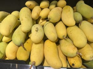 A close-up view of a pile of ripe mangoes in various shades of yellow and green, with some showing slight blemishes.