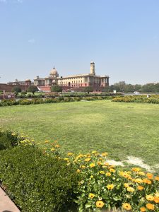 A lush green lawn adorned with vibrant yellow flowers in the foreground, leading up to an impressive historical building in the background. 