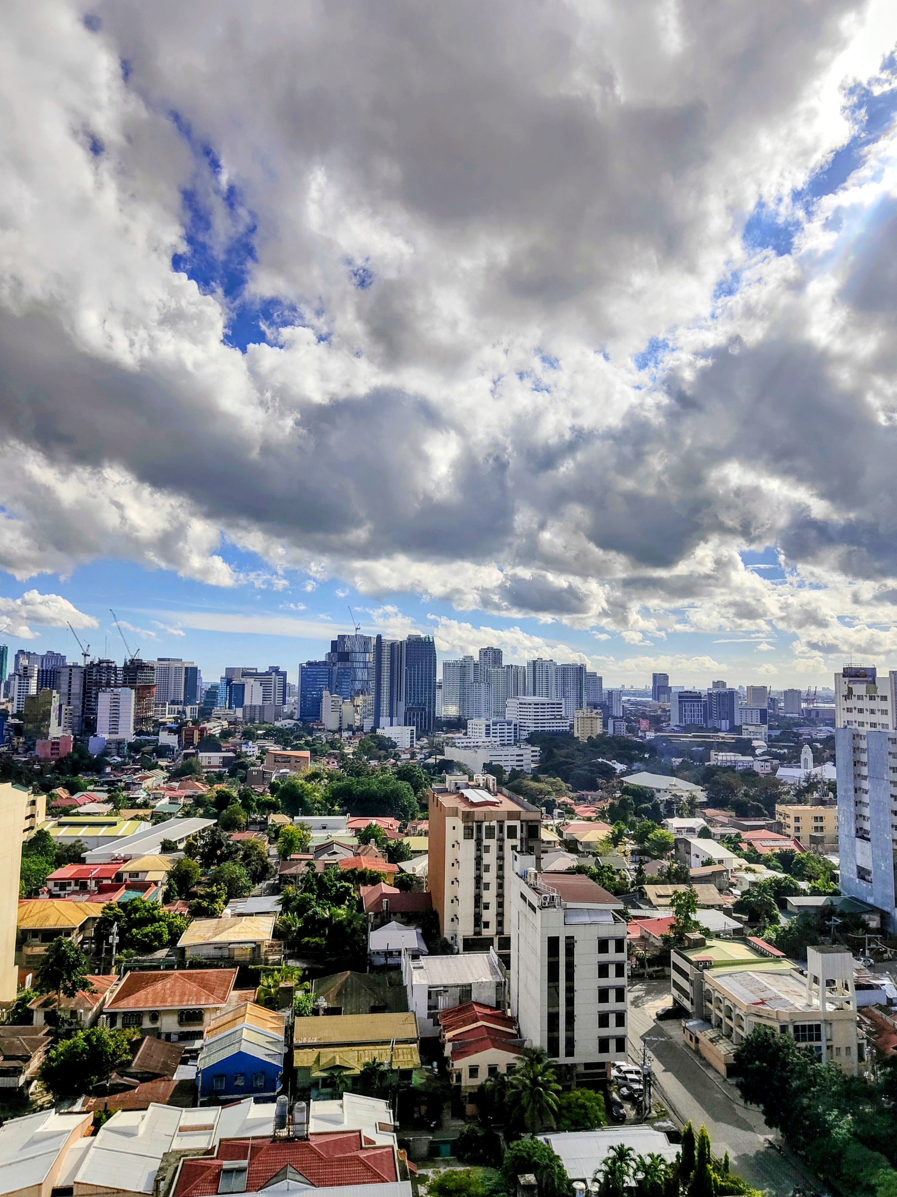 A dramatic view of Cebu City, Philippines, showcasing a mix of low-rise neighborhoods and modern high-rises under a sky filled with thick, textured clouds. The scene captures the vibrant contrast of urban life and tropical weather.