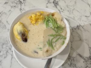 A bowl of sweet dessert with durian, corn, green jelly, and coconut milk.
