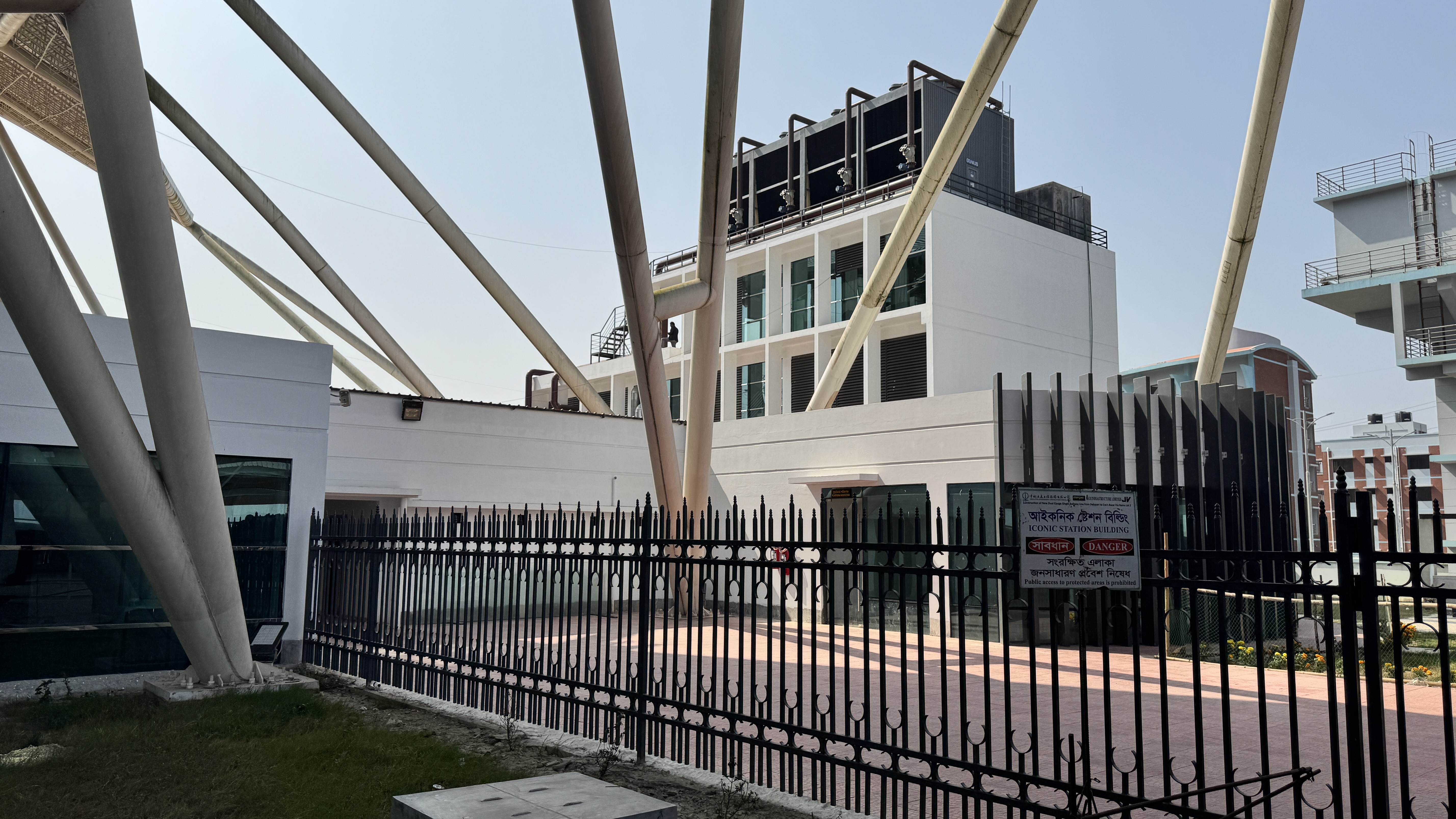 A modern building with a white facade and large glass windows is surrounded by a black wrought-iron fence.