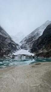 A rugged mountain landscape features steep, snow-capped peaks shrouded in mist
