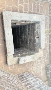 A view of a square, stone-lined opening leading down into a dark, brick-lined shaft