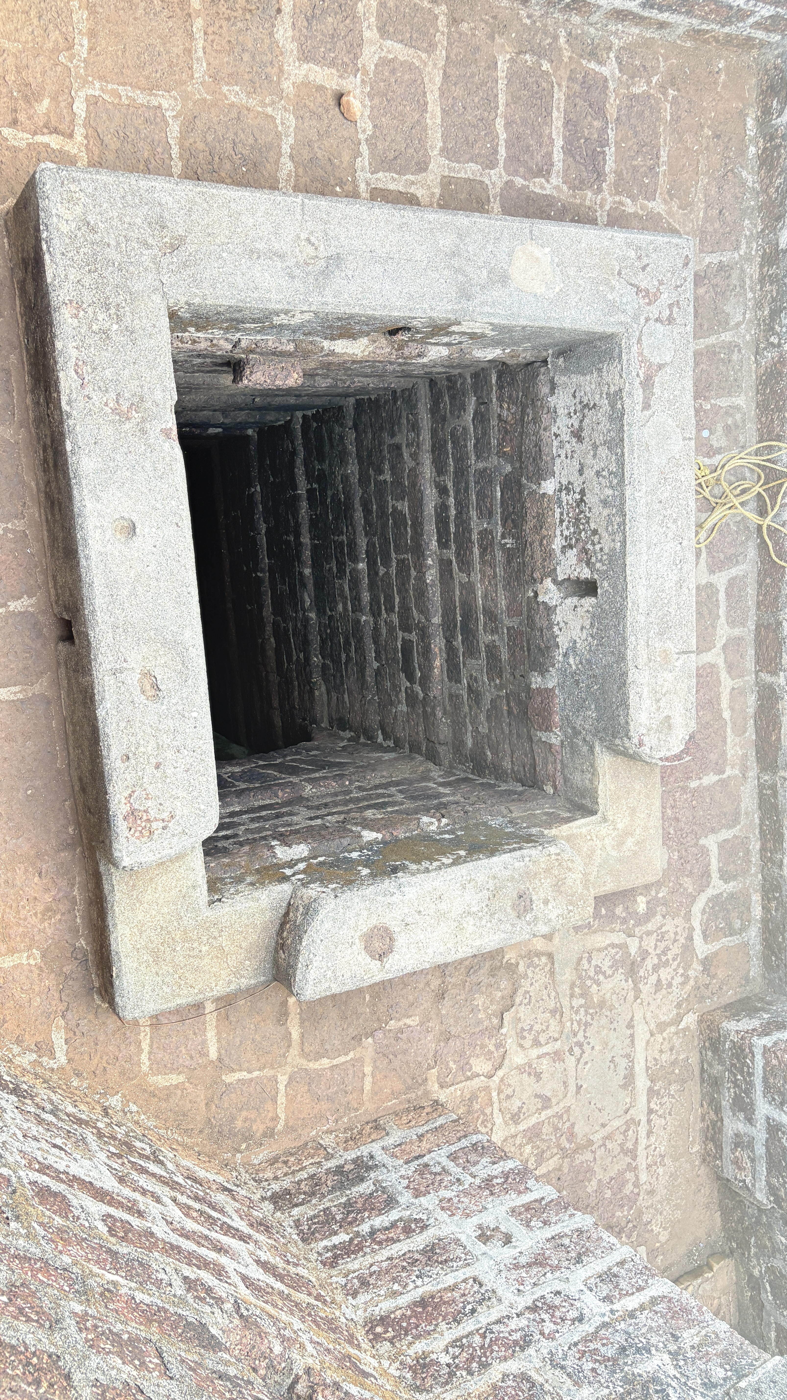 A view of a square, stone-lined opening leading down into a dark, brick-lined shaft