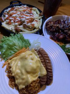 A plate of food featuring two grilled sausages topped with melted cheese, served over a bed of noodles.