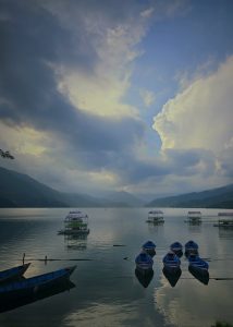 A serene Fewa lake scene with calm waters reflecting the sky and surrounding mountains