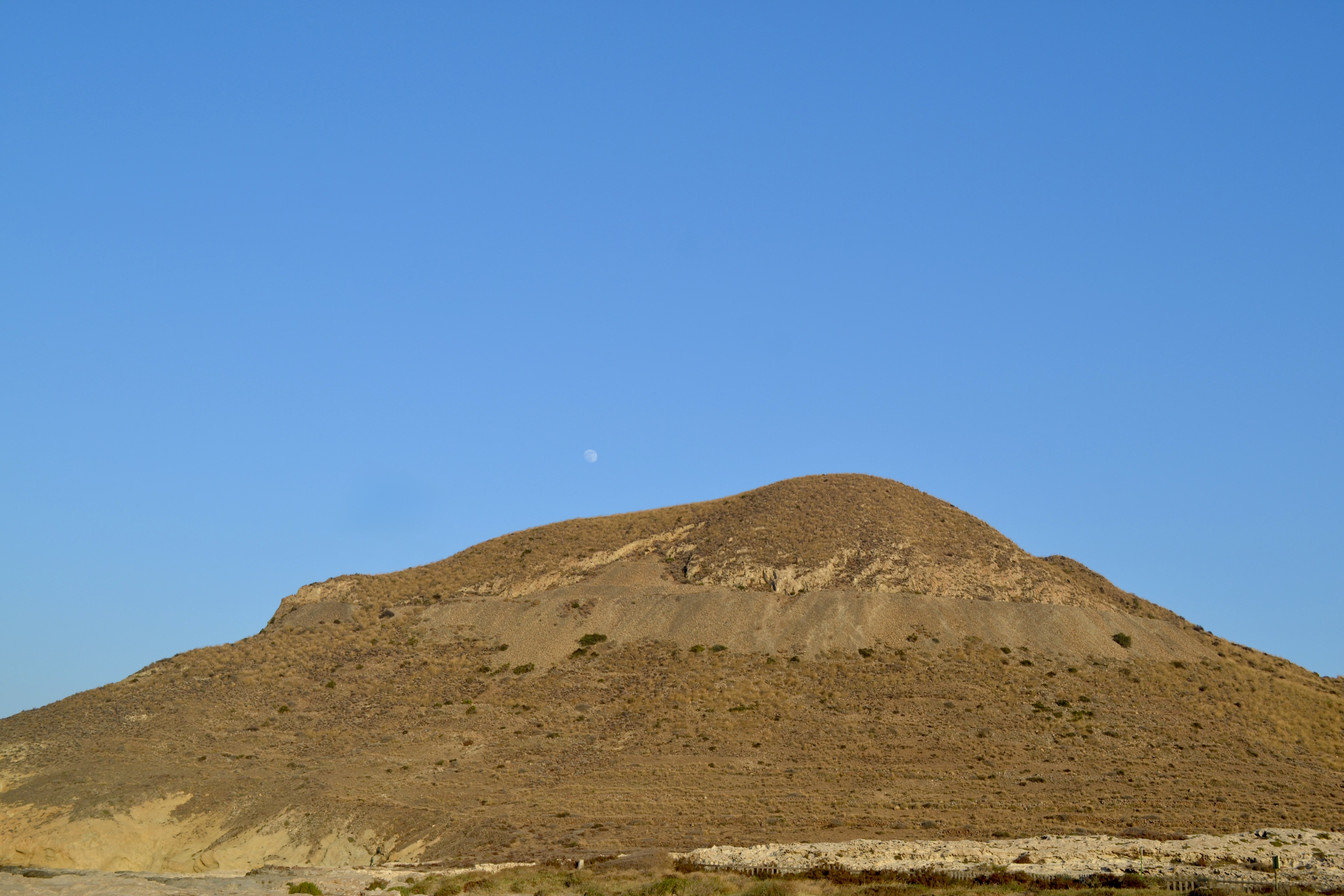 A dry brown hill under a clear blue sky with a faint moon above, captured in Tenerife, Spain
