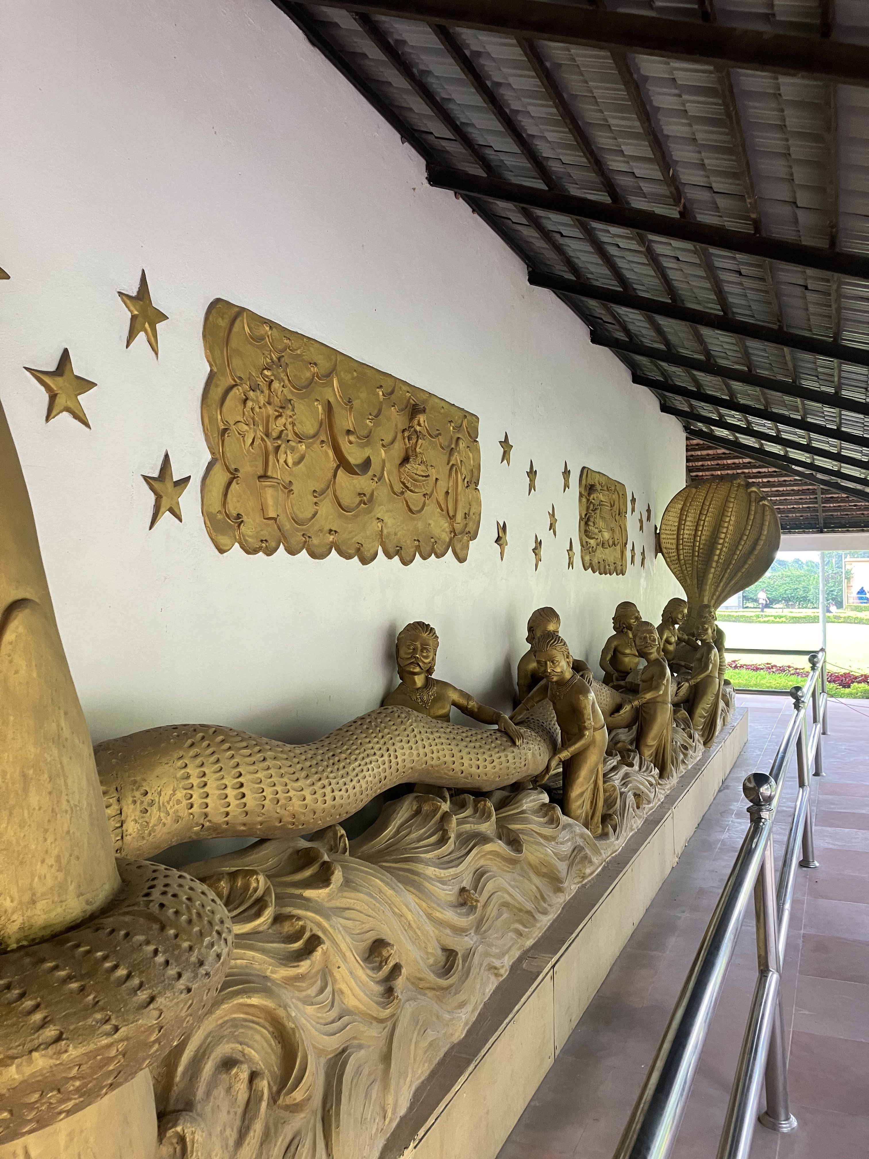 A long, intricately carved relief sculpture featuring figures of children and a serpent, depicted in a flowing wave-like pattern. The figures are shown actively engaging with the serpent, with some holding onto it.