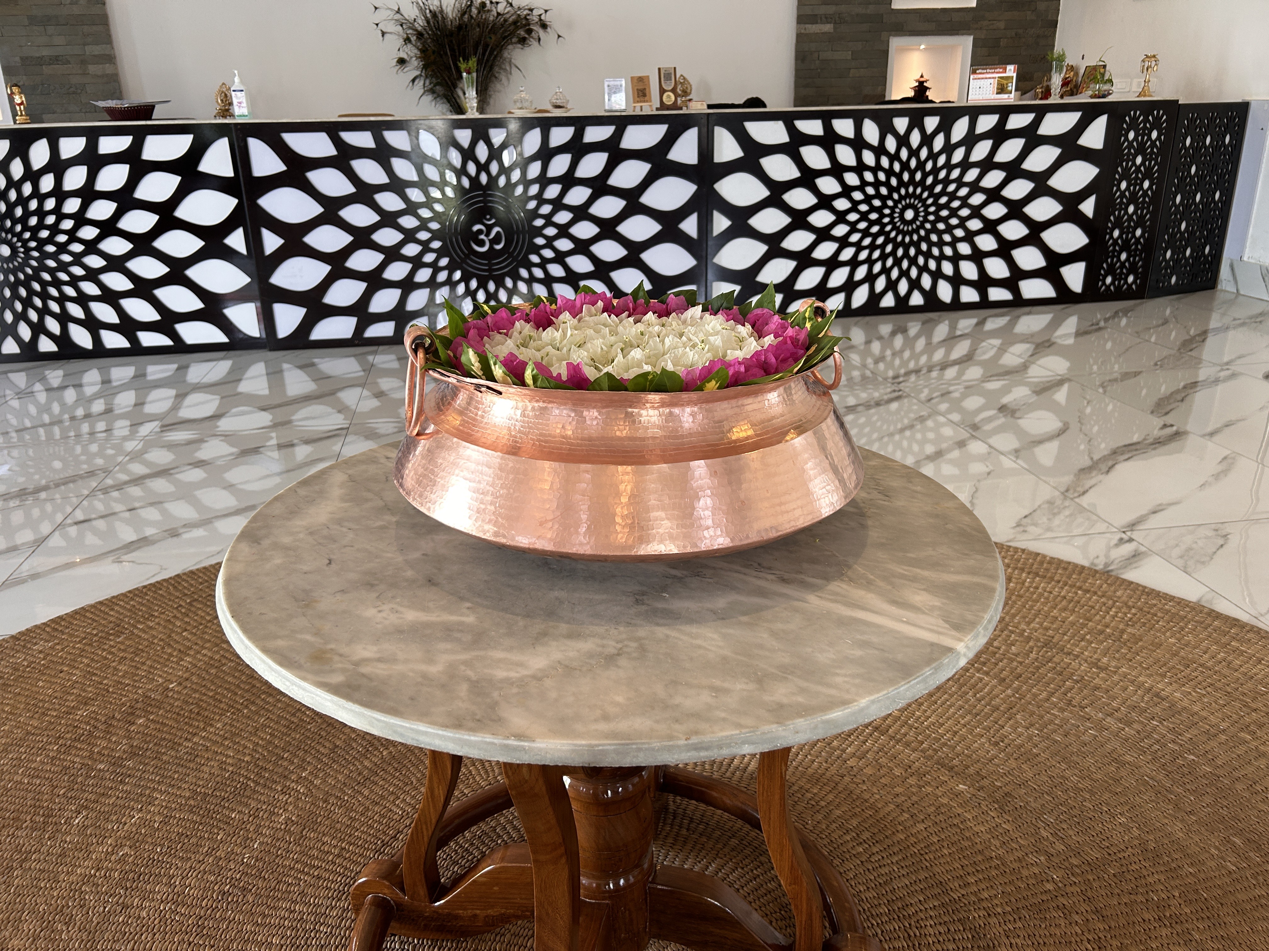 A copper bowl filled with flowers sits on a round marble tabletop, which is supported by a wooden base.