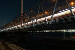 A night view of subway train tracks stretching across a railway bridge in Tokyo, with trains speeding through the city lights.