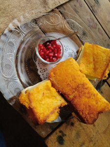 Three golden sandwiches sit on a clear etched plate, centered with a bowl of pomegranate seeds. Set on a rustic wooden table with burlap for a cozy touch.