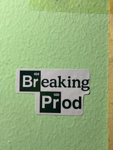 A sticker on a textured light green wall features the text &quot;Breaking Prod&quot; in a stylized font.