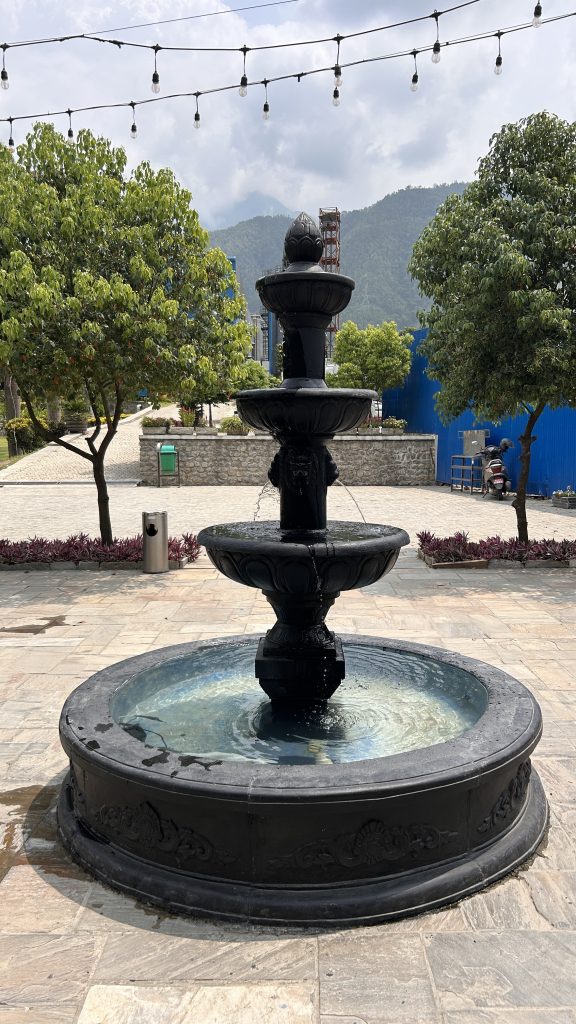 A black stone fountain with four tiers, water gently spilling from each level into a circular basin.