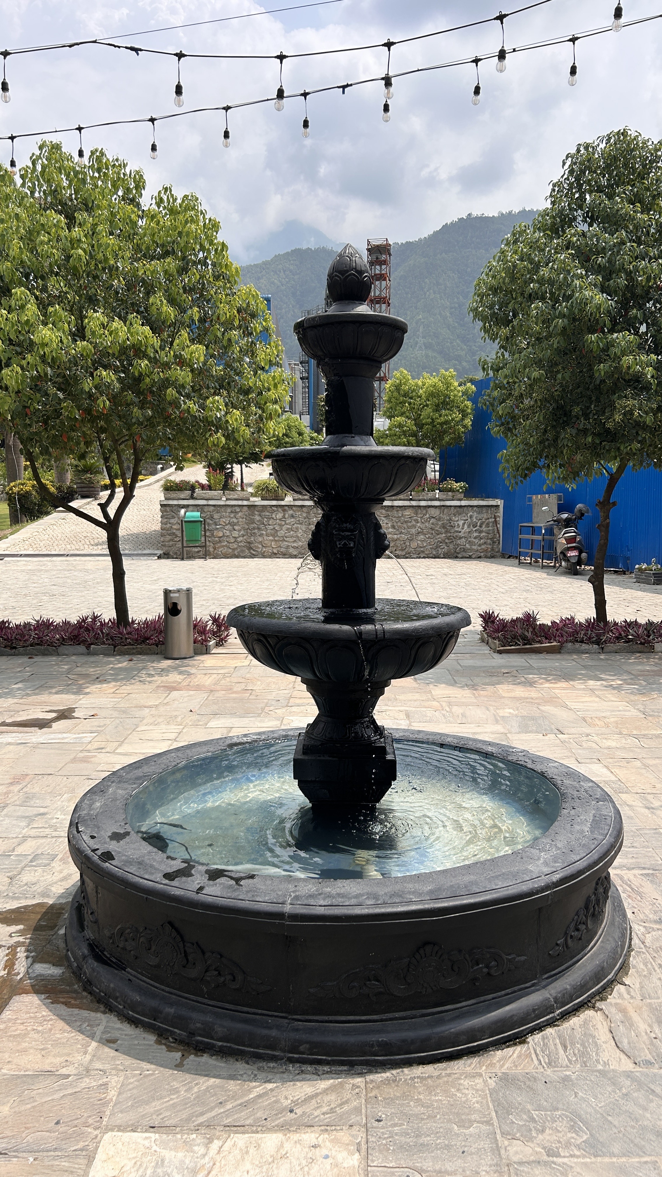 A black stone fountain with four tiers, water gently spilling from each level into a circular basin.
