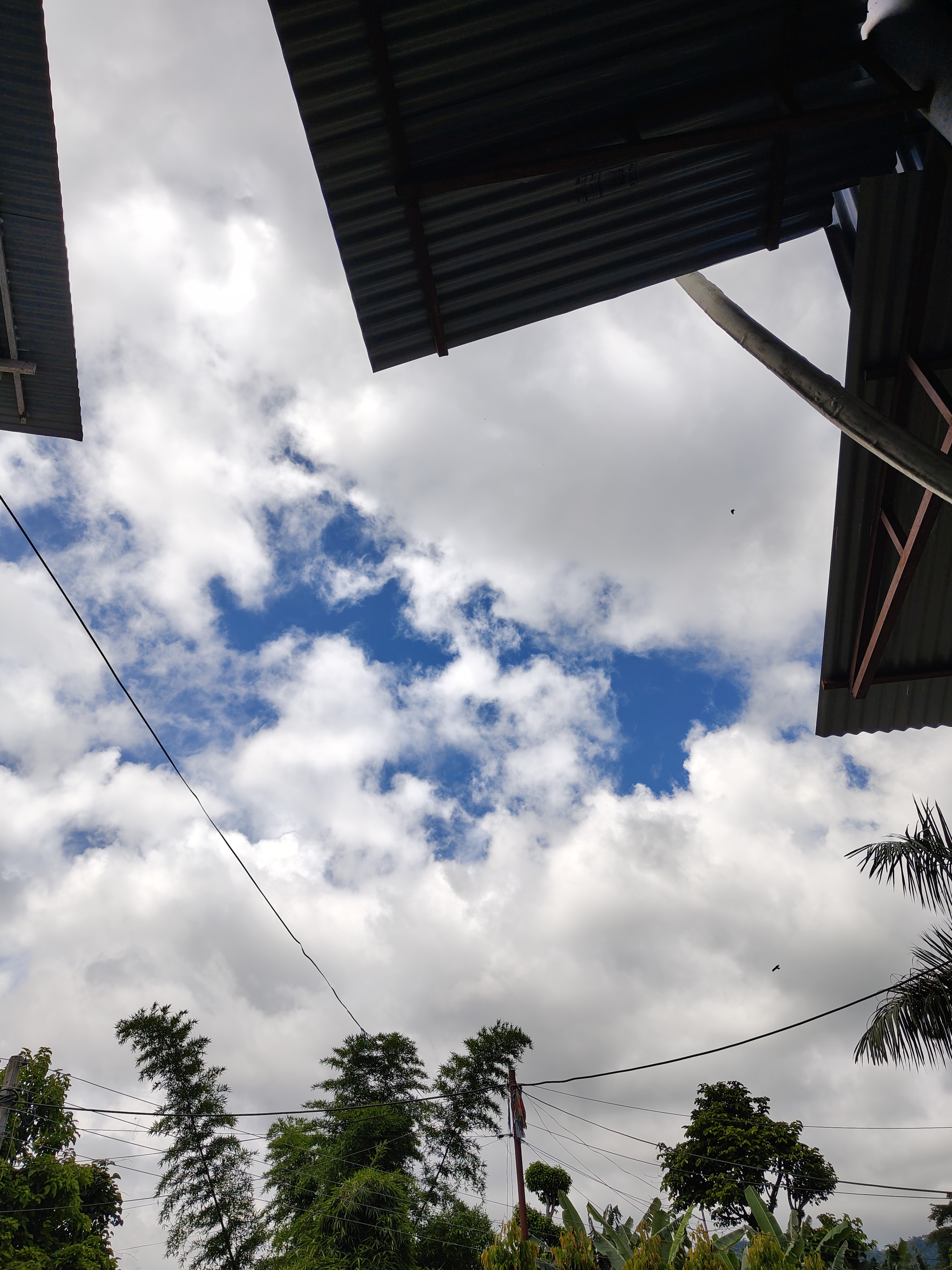 A view of a partially cloudy sky framed by the edges of two metal roofs.