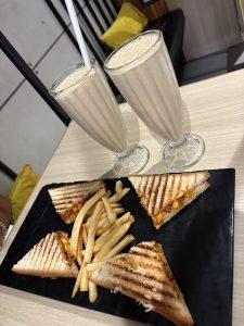 Breakfastwith two glasses of milkshake, a plate containing four toasted sandwiches and sme crispy french fries.
