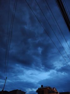 A dark blue sky filled with thick, swirling clouds; overhead power lines crisscross the scene.