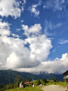 A scenic landscape featuring a blue sky filled with fluffy white clouds, alongside lush green mountains in the background.