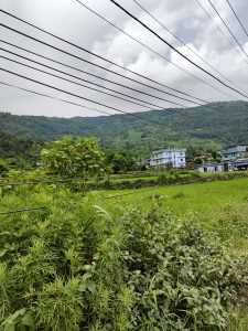 A scenic view of green hills under a partly cloudy sky, with electric wires stretching across the image
