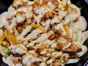 A loaded bowl of French fries topped with juicy chicken, creamy cheese sauce, and spicy dressing—street food delight from Kozhikode, Kerala.