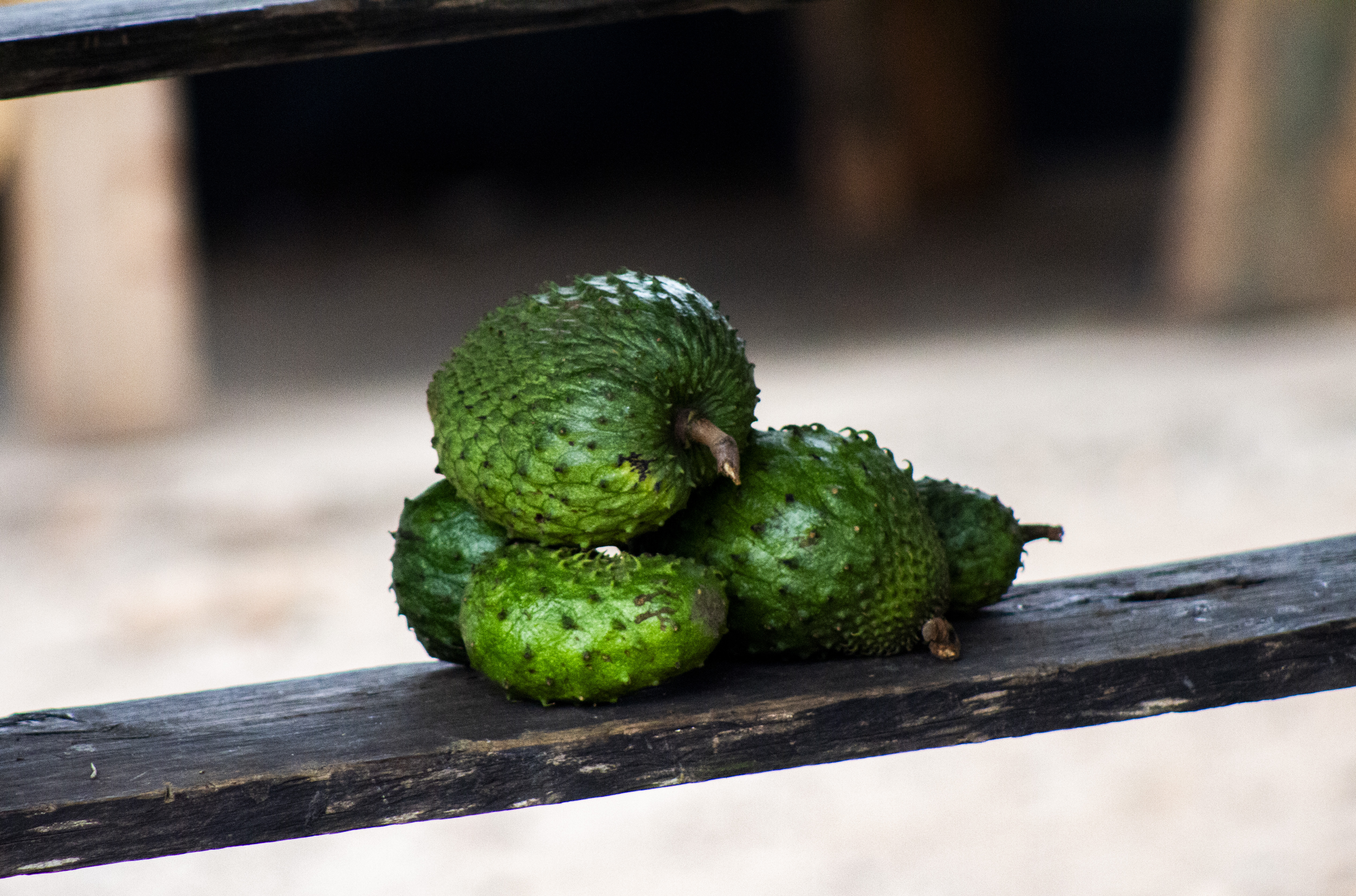 Spiky green soursop fruits stacked on a wooden shelf at a rustic village market in Uganda, with a blurred rural backdrop.