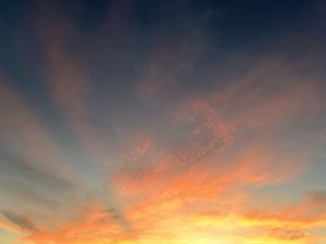 A vibrant sunset sky filled with swirling clouds in shades of orange, red, and deep blue, creating a dramatic and colorful backdrop.