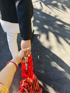  A man and woman in traditional Nepali attire hold hands while walking together as a bride and groom.
