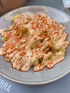 A close-up view of a plate of Patatas Bravas crispy potato chips or fries topped with a creamy sauce and a generous dusting of paprika.