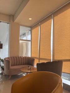 A cozy interior space with large windows covered by light brown shades allowing soft sunlight to filter in.