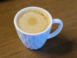 A close-up of South Indian filter coffee with creamy froth, served in a white cup—captured indoors in Kozhikode, Kerala.
