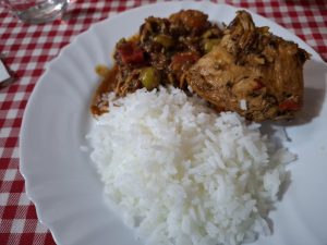 Turkey stew with gravy on the side and white rice, served on a white plate over a red-and-white tablecloth on the table.