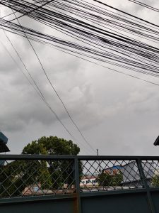 A view of a cloudy sky filled with shades of grey, intersected by numerous black electrical wires.