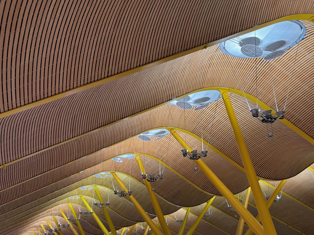 A close-up view of the Madrid airport ceiling, featuring a series of undulating wooden panels with vertical grooves.