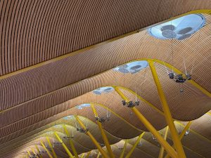 A close-up view of the Madrid airport ceiling, featuring a series of undulating wooden panels with vertical grooves.
