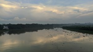 A tranquil river scene at dusk, featuring calm water that reflects the cloudy sky above. 
