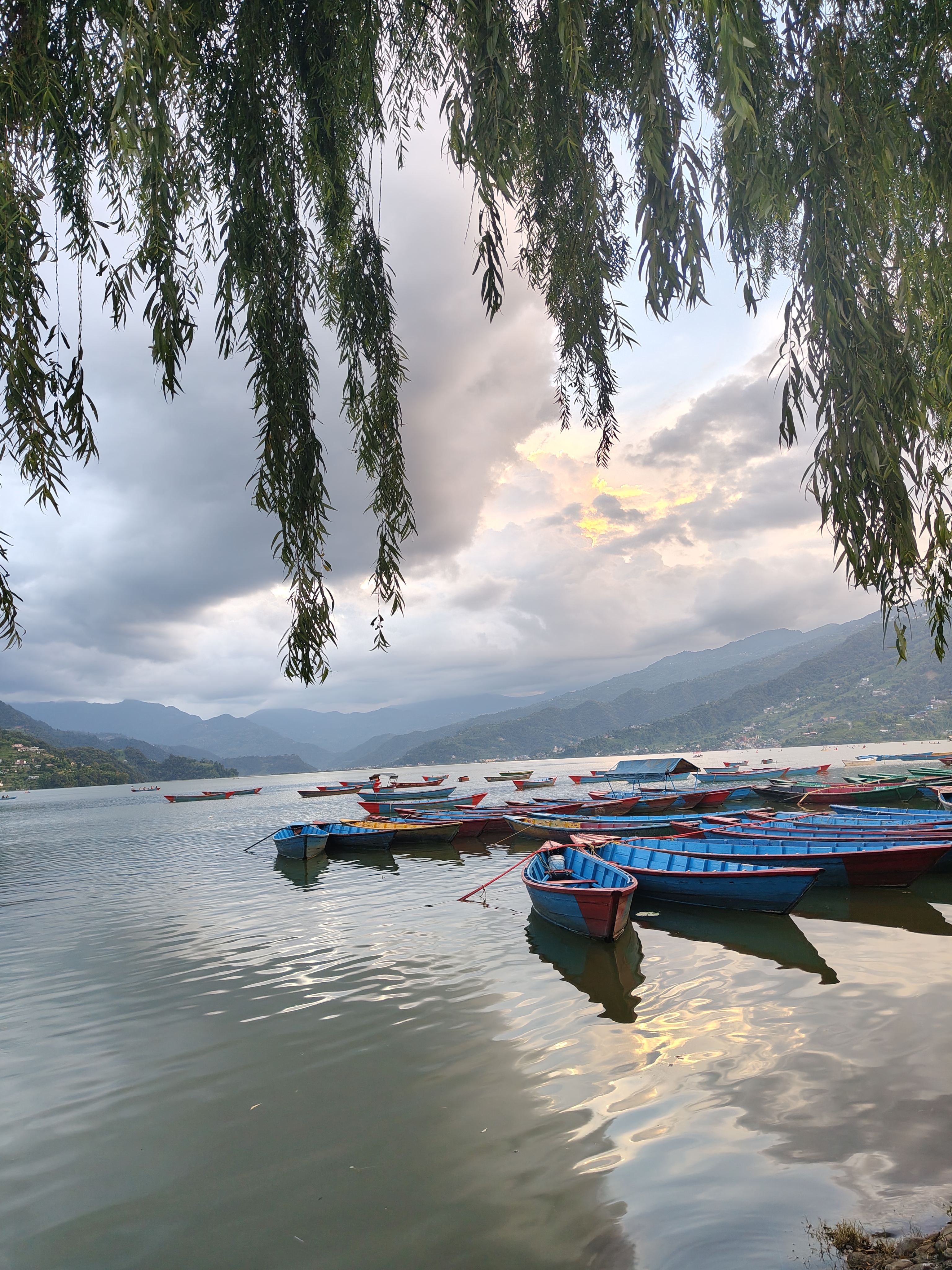 A serene lake scene at sunset, featuring several colorful wooden boats anchored in calm waters