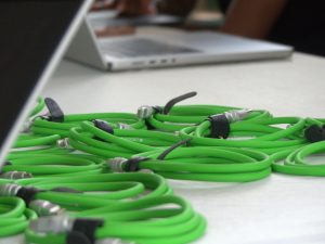 A collection of coiled green Jetpack USB-C cables, intended as giveaways for attendees, displayed on a table at WordCamp Masaka 2025. A laptop is partially visible in the upper background.
