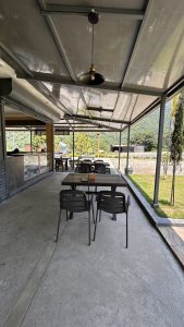 A spacious outdoor seating area at a café or restaurant, featuring several black metal chairs and tables arranged on a grey concrete floor. 