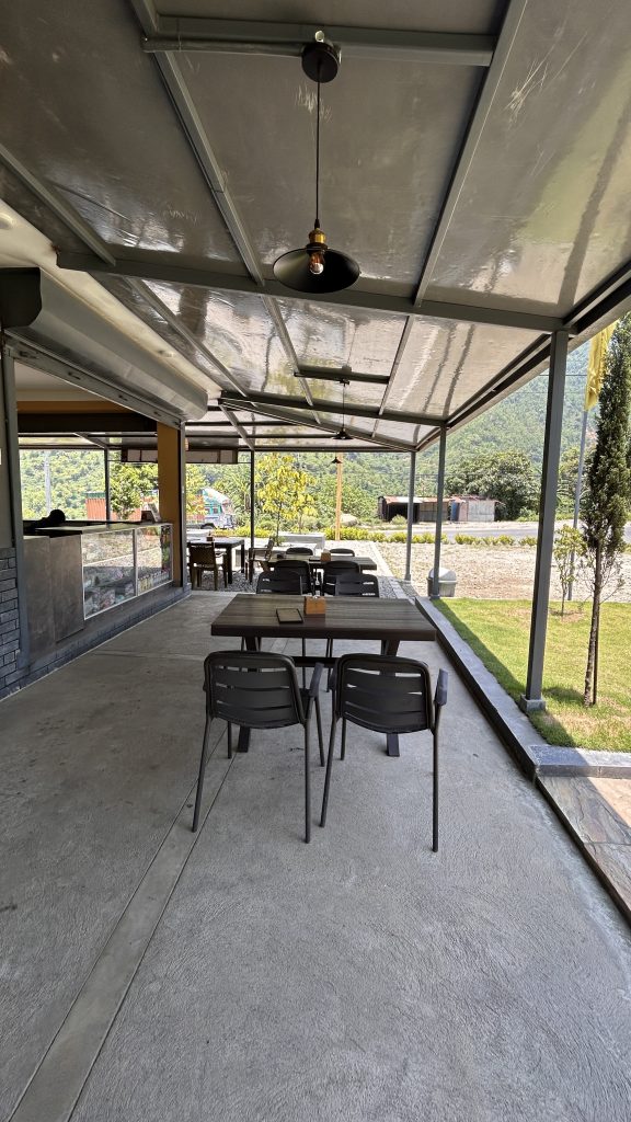A spacious outdoor seating area at a café or restaurant, featuring several black metal chairs and tables arranged on a grey concrete floor.