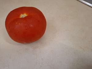 A ripe tomato sits on the kitchen counter, glistening with moisture.
